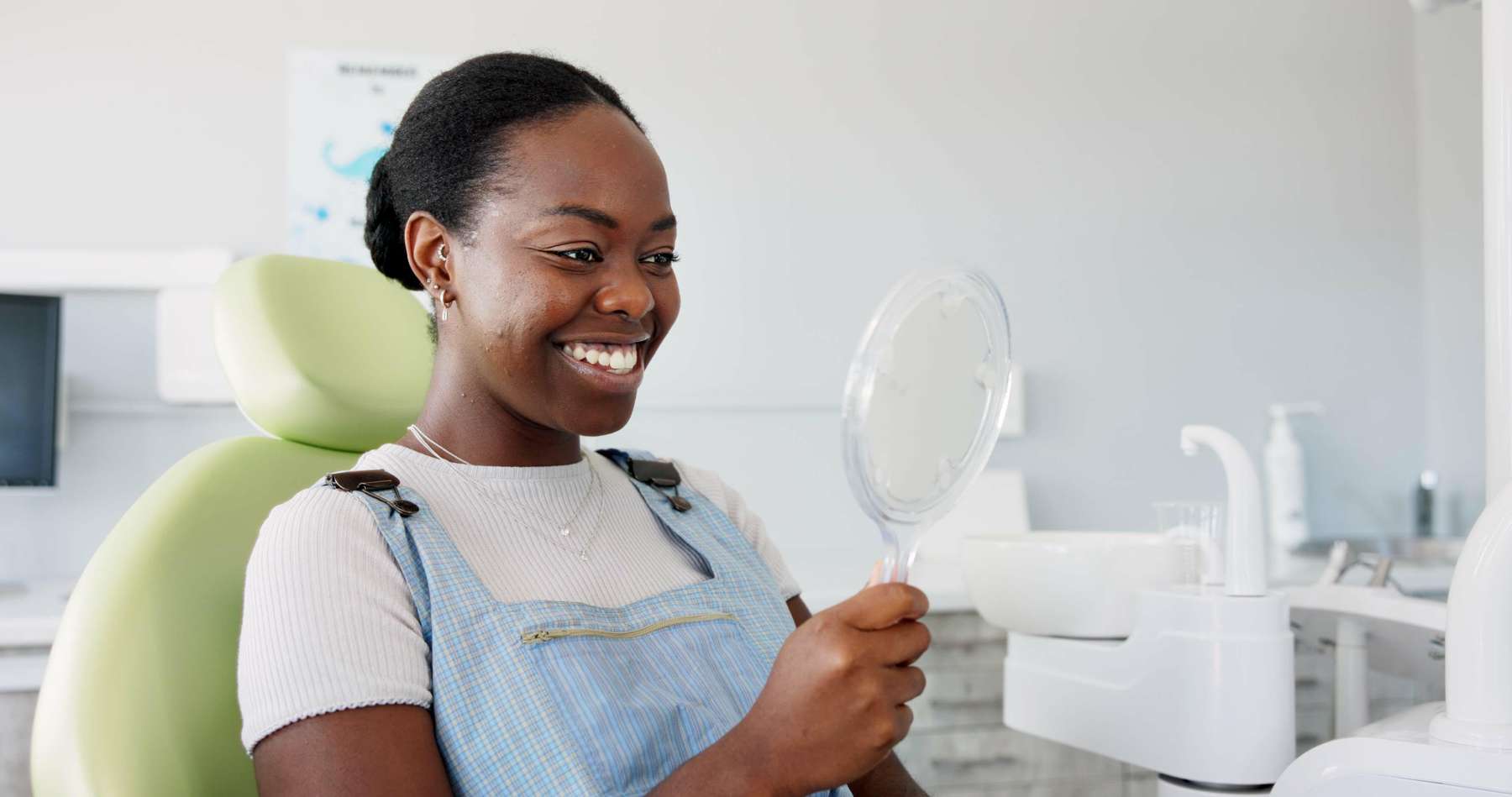 Black woman looking at her teeth in a handheld mirror at a dentist office, huntsville al
