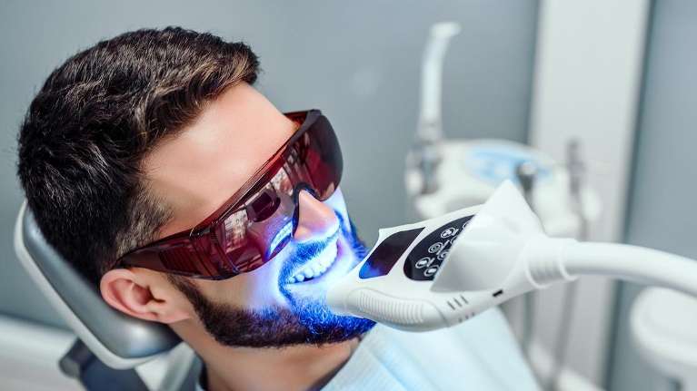 Man receiving professional teeth whitening treatment with LED light at a dental office