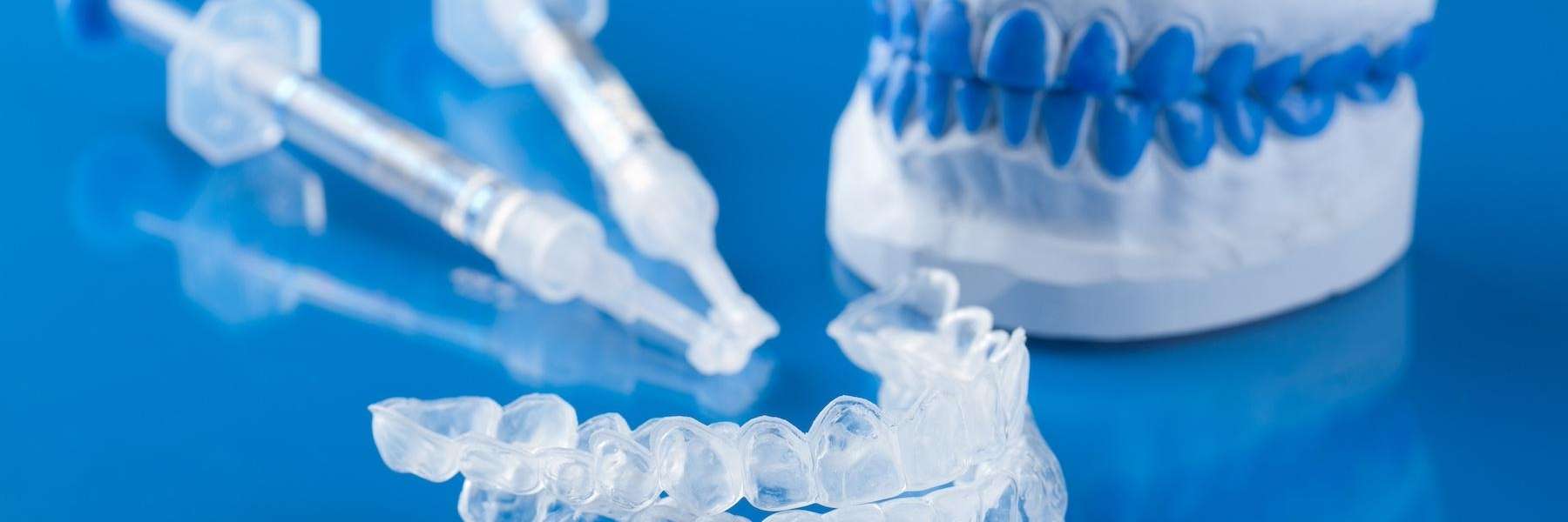 Teeth whitening trays with gel syringes and dental model on blue background