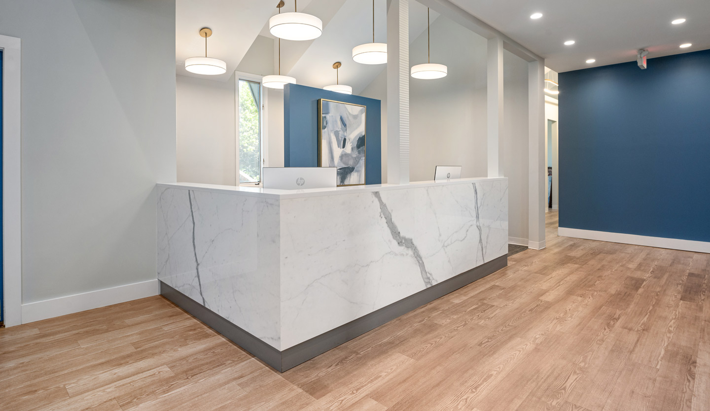 Twickenham Family Dentistry A sleek reception area featuring a white marble front desk, pendant lighting, and blue accent walls. The space is bright and welcoming.